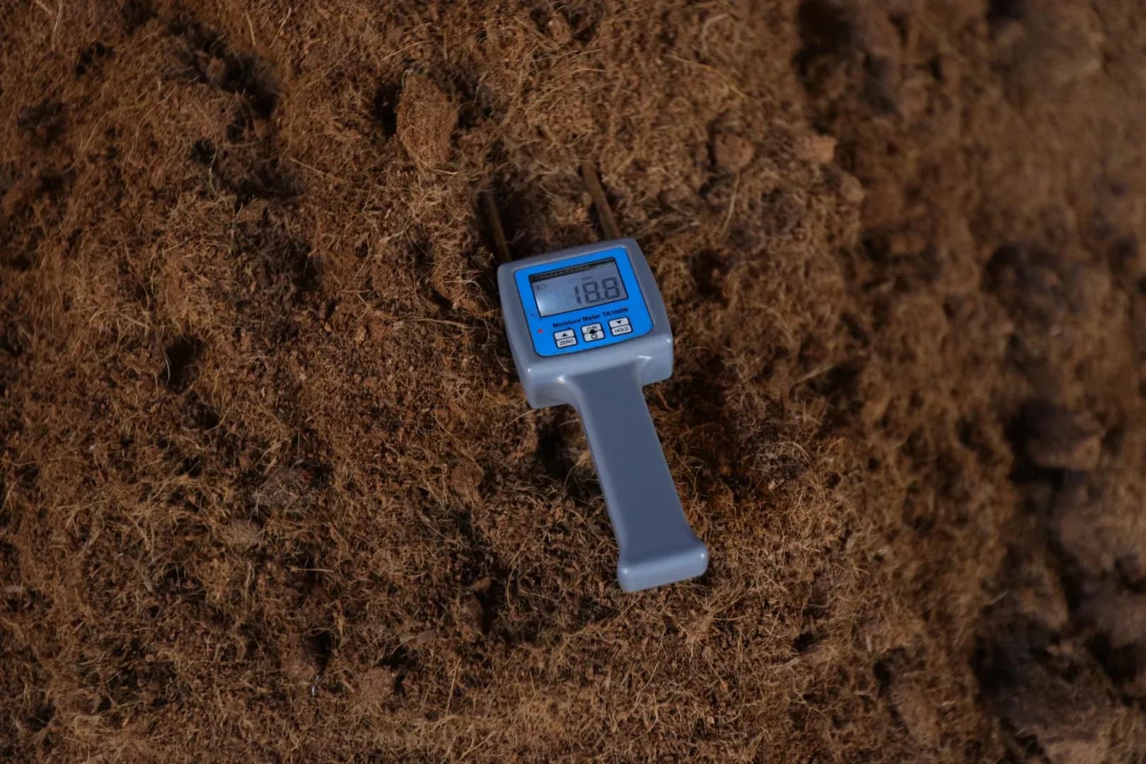 Digital moisture meter measuring moisture content in coco coir substrate during quality testing.