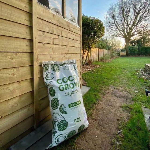 A large, black 50 litre bag with green text reading "COCO GROW 50L" and a palm tree illustration, filled with loose coco coir growing medium.