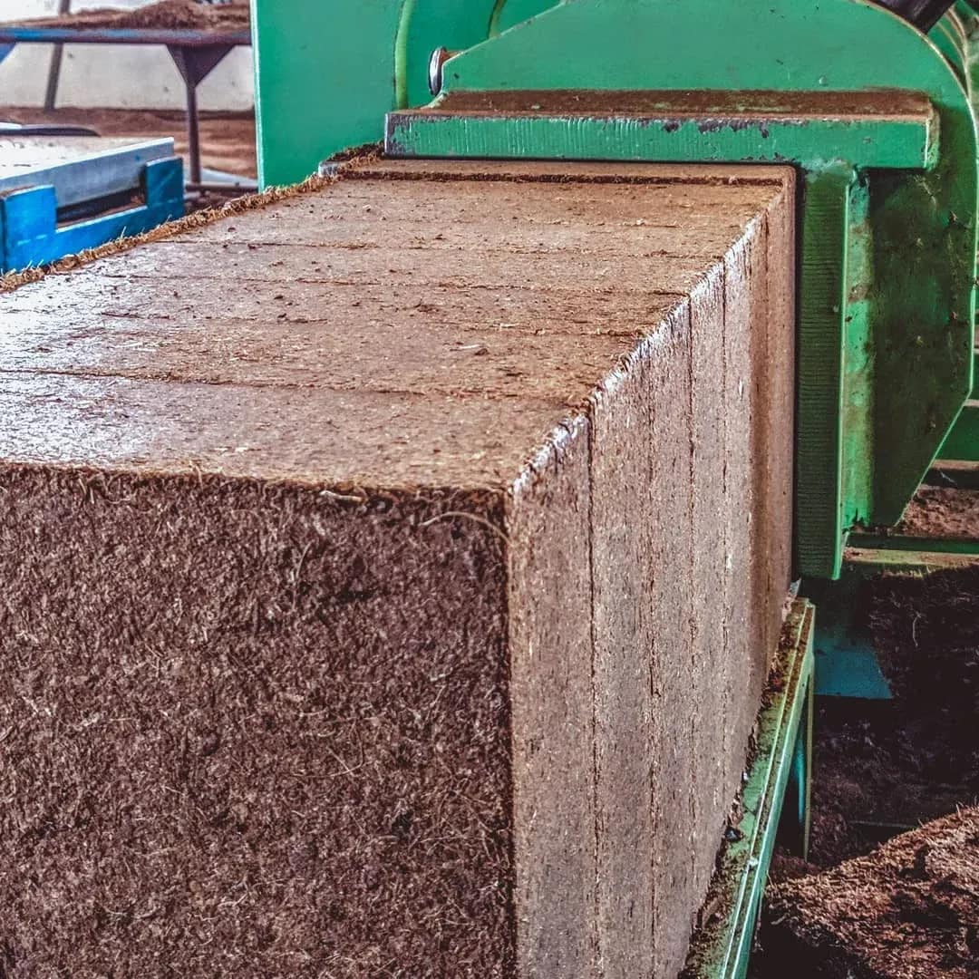 Compressed coco coir block being pressed by manufacturing equipment during processing